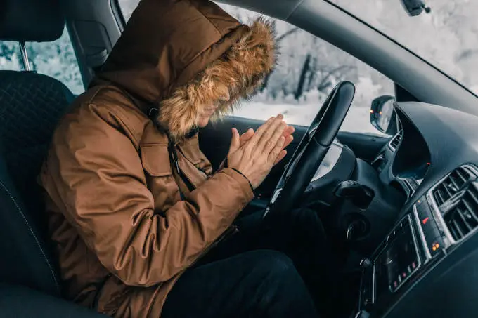 Man In Down Jacket Tries To Keep Warm And Not Freeze In His Stalled Car In Winter. The Concept Of A Dangerous Accident Or Heater Failure In The Cold Season
